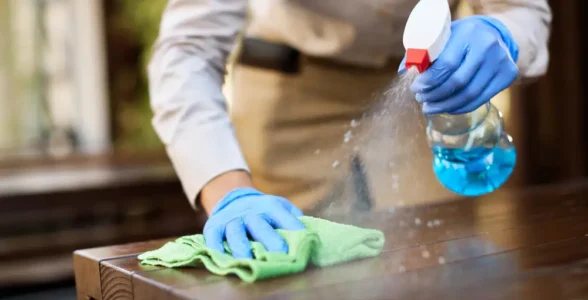 A person using a COSHH spray to clean a wooden surface.