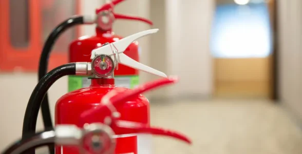 A photograph of three fire extinguishers along a long white corridor.