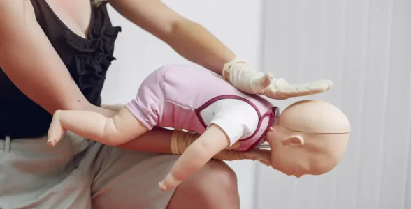 A person is practising stopping choking in a child with the first aid course instructor from 4JH there too.